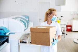 Masked lab employee carrying a box